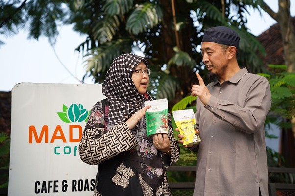 senseisugimotokunjungismart3 dompet dhuafa Two people in head coverings compare coffee bags in front of a cafe sign that reads MAD COFFEE/Cafe & Roastery as they chat outside.