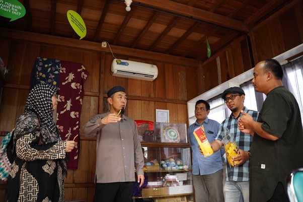 senseisugimotokunjungismart5 dompet dhuafa Five adults in a wooden-room workshop; a man in a gray shirt and cap gestures as others listen, two holding snacks in the background.