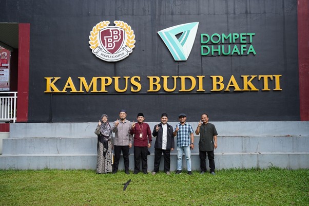 senseisugimotokunjungismart9 dompet dhuafa Group of seven people posing in front of a black wall with 'KAMPUS BUDI BAKTI' in gold and campus logos above.