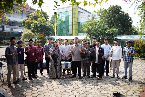 senseikesmart4 dompet dhuafa Group of students and a faculty member posing in a campus courtyard with a modern glass-front building in the background.