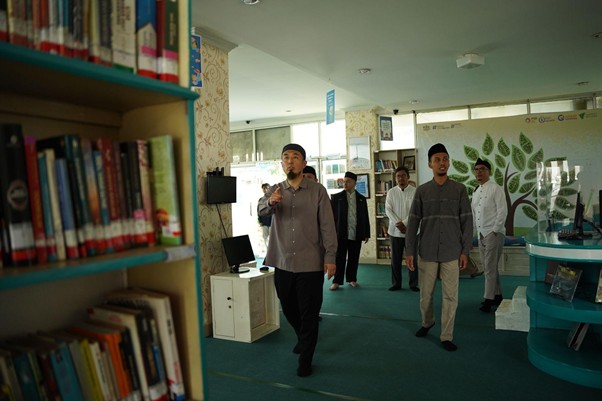 senseikesmart5 dompet dhuafa Man with a microphone leading a group in a library; shelves of books on the left and a tree mural on the back wall.