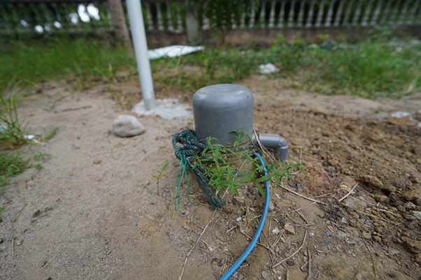 sumur bor di bireun aceh 4 dompet dhuafa Outdoor irrigation valve/post with a blue hose on dirt, weeds growing nearby.