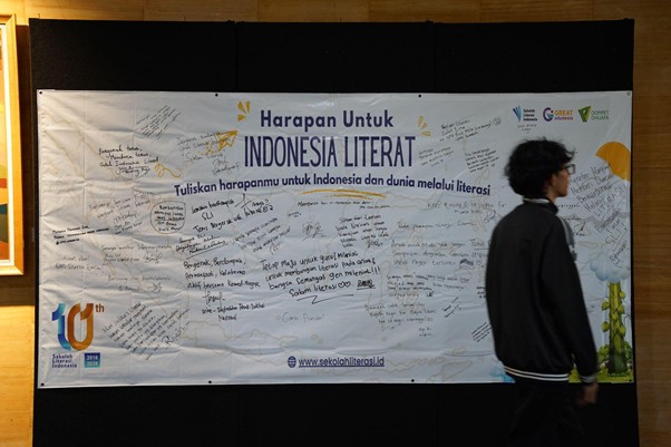 yatim penakluk speech delay 4 dompet dhuafa Banner titled'Harapan untuk Indonesia Literat' filled with handwritten messages, with a man walking past on the right.